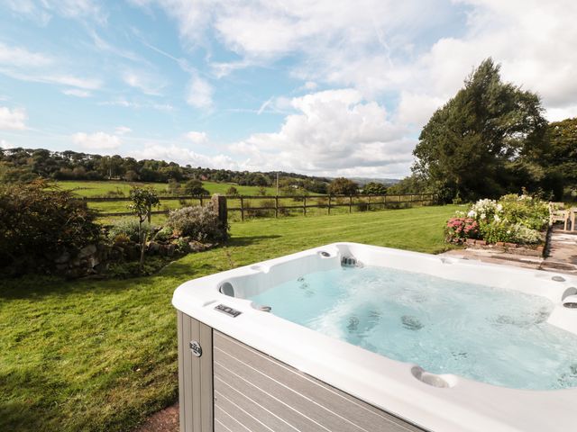 An outdoor hot tub in a garden with grass and flowers at Lee House Cottage in Cheddleton