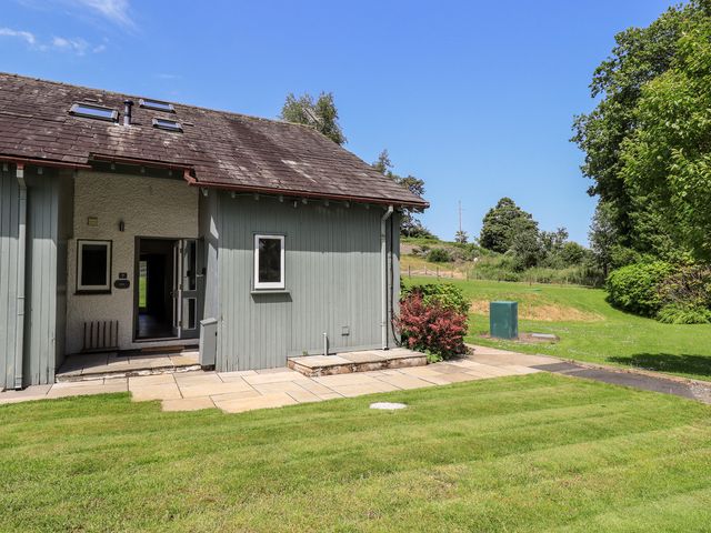An outdoor view of a building with a patio and grass at Yew - Woodland Cottages Bowness-On-Windermere