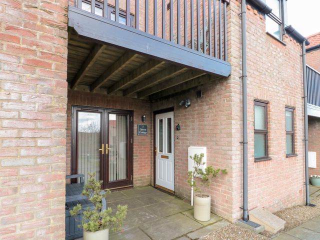 An exterior view of a brick building with a white door and glass double doors under a wooden balcony at Grove Cottage Whitby
