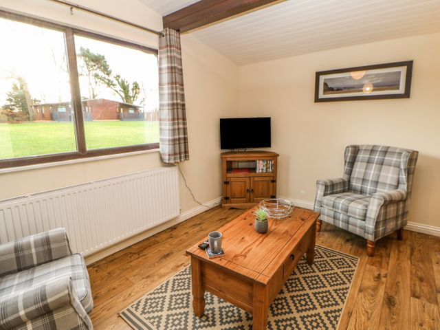 A living room with plaid armchairs wooden coffee table television and window showing grass outside at Snowdrop in Saltburn-by-the-Sea