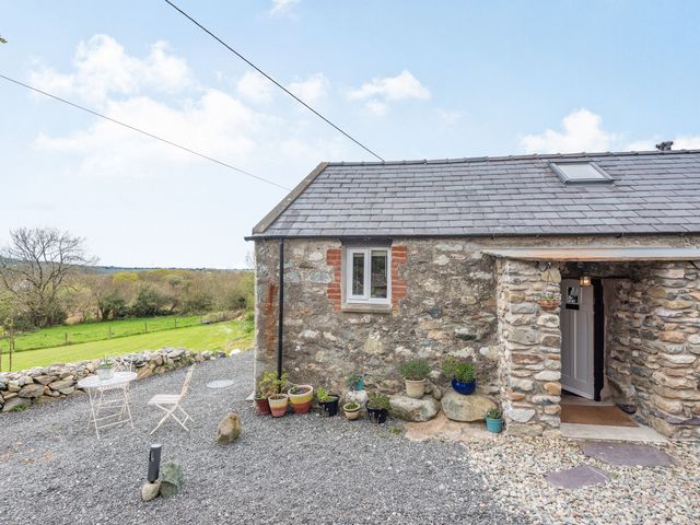 Stone cottage exterior with potted plants and outdoor seating on gravel at Celyn Farm Cottage in Deiniolen near Llanberis
