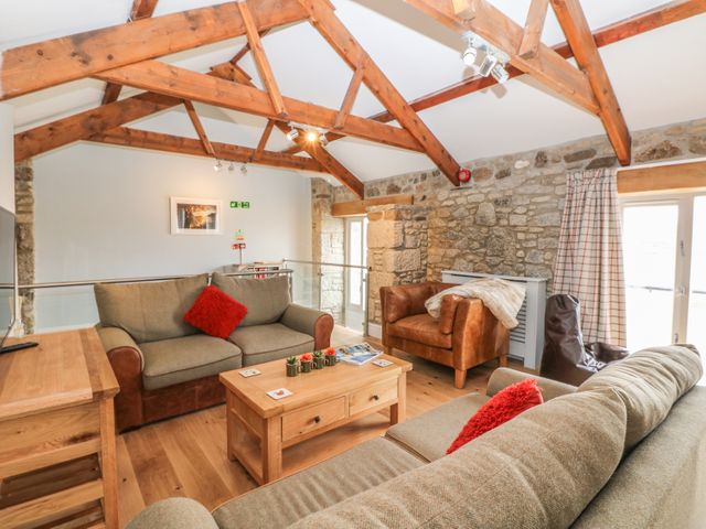A living room with wooden beams stone walls sofas and a coffee table at Helford in Treverva near Constantine