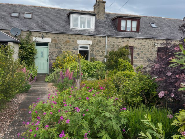 A building with a green door and flowers in the garden at 5 Distillery Cottages, Banff