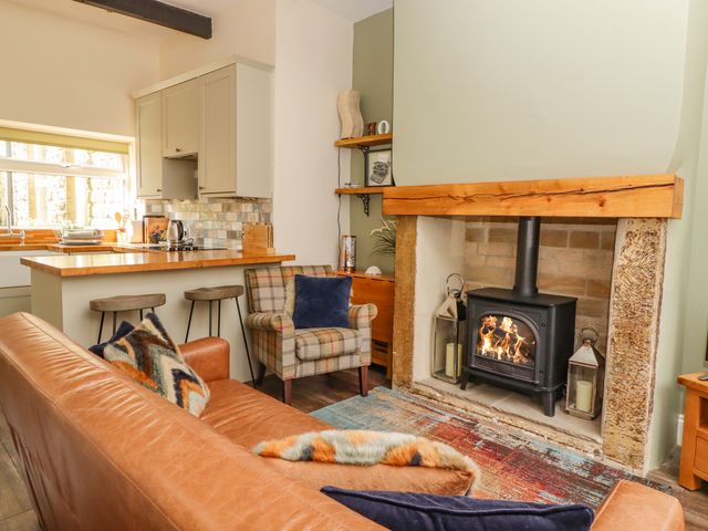 A living room with a leather sofa pillows an armchair a fireplace and a kitchen counter with bar stools at Maria Cottage in Haworth