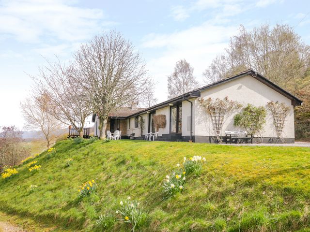 A single-story house with outdoor seating on a grassy hill with trees and flowers at Strath Glass View at Hill House in Cannich