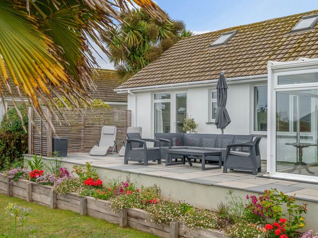 An outdoor patio with wicker chairs a table an umbrella and flower beds at Wide Horizons in Coverack