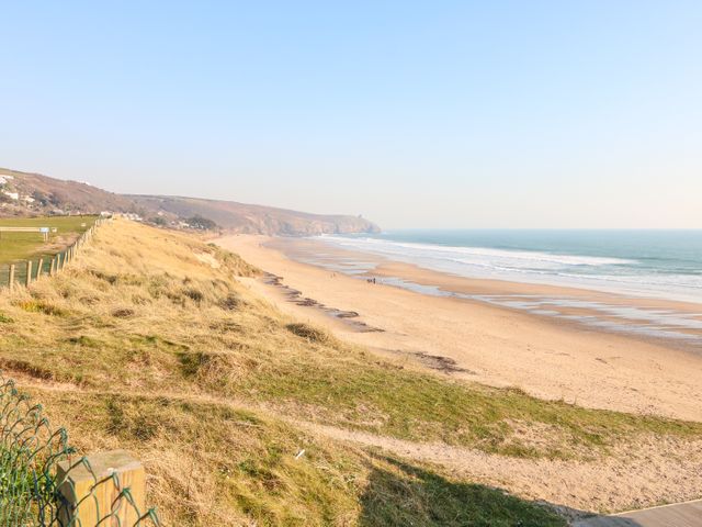 A sandy beach with waves and a grassy cliff with a fence at Bre An Mor in Praa Sands