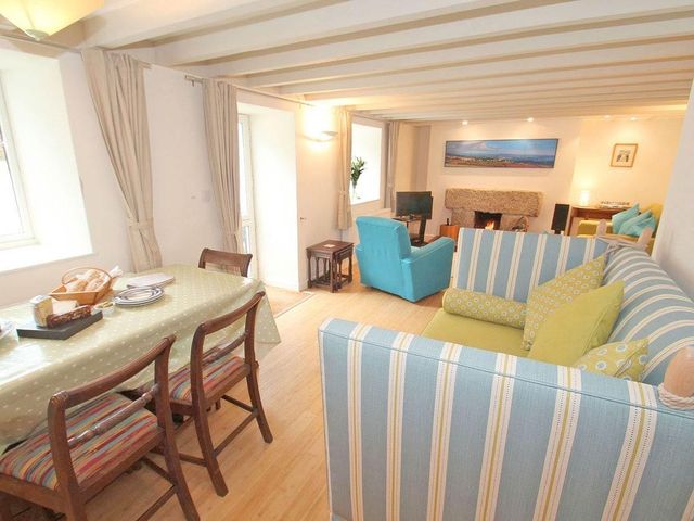 A living and dining room with a striped sofa a blue armchair a dining table with chairs and a fireplace at White Duck Cottage in Hayle