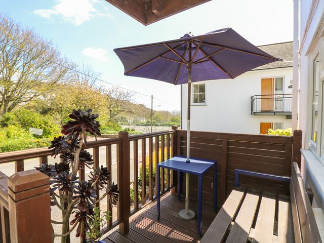 A small balcony with a bench table with umbrella and potted plant overlooking a street at Seascape in Porthcurno