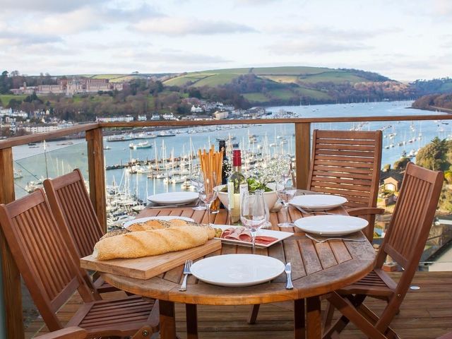 A wooden outdoor dining table with bread, wine, plates and glasses overlooking a marina with boats at Totherside in Kingswear