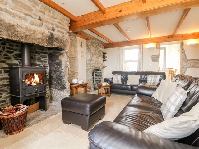 A living room with a wood burning stove two leather sofas an ottoman and stone walls at Boslow in St Just