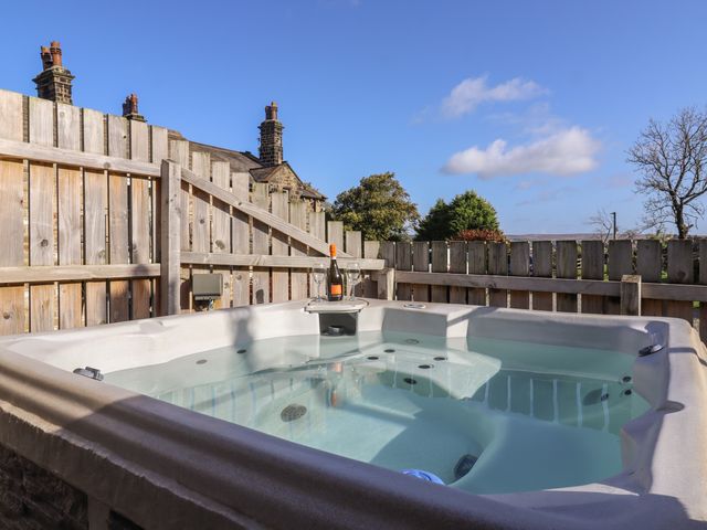 An outdoor hot tub with a bottle of wine and two glasses on a wooden tray by a wooden fence at The Old Hen Shed in Hainworth near Haworth