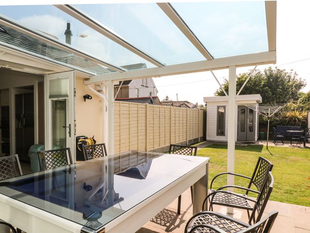 An outdoor covered patio with a table and chairs overlooking a fenced garden with a shed and a clothesline at Ridgeback House in Mullion