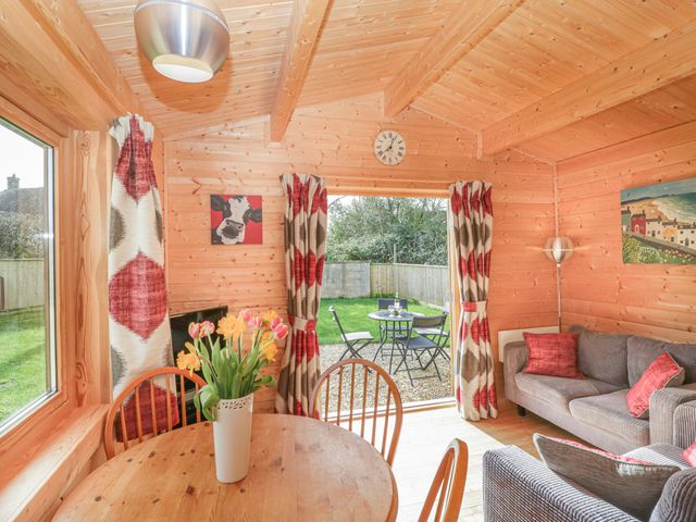 A wooden interior room with a round table and chairs a sofa and armchair red and beige curtains and a door leading to a garden at The Shippen in Merriott
