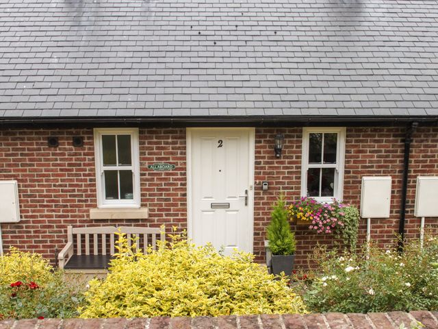 A brick house entrance with a white door numbered 2 two windows flowers and a bench at All Aboard in Whitby