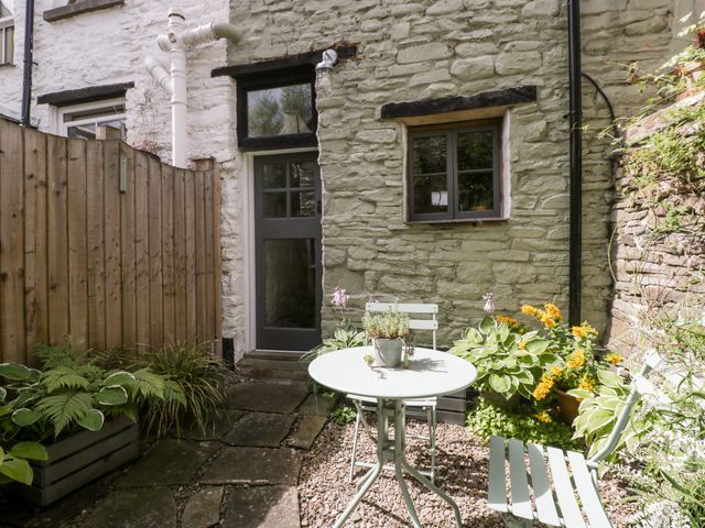 A small outdoor patio with a round table and two chairs surrounded by plants and a stone wall at 7 Bell Street in Talgarth