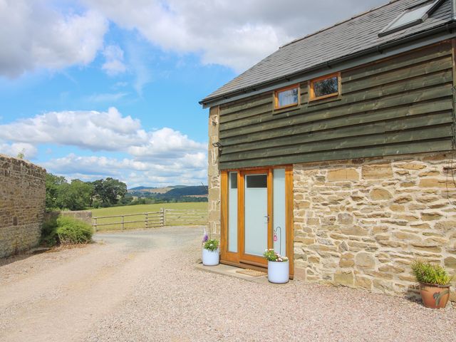 An outdoor view of a stone building with a wooden door and gravel driveway at The Hay Loft in Craven Arms