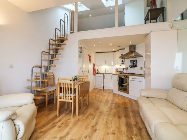 A kitchen and dining area with wooden floors a small wooden dining table and chairs a metal and wood spiral staircase and white cabinets at 10 Oceanside in Ilfracombe