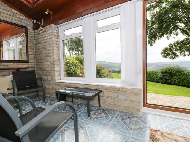 A sunroom with two black chairs a small glass table and a window and door showing a garden at Upper Highlees Farm in Midgley near Luddenden