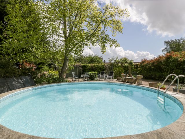 An outdoor swimming pool with metal handrails surrounded by trees and garden furniture at The Granary in Edington near Street and Glastonbury