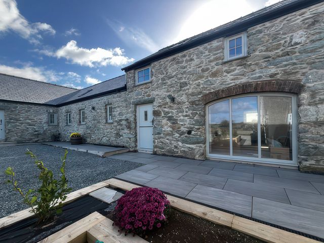 An outdoor area with a stone wall and flower bed at Storws Tanrallt Llanfachraeth