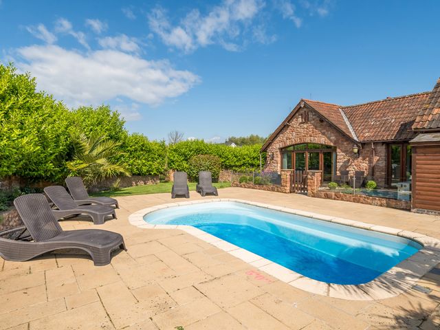An outdoor pool with six lounge chairs and a stone house in the background at The Old Byres in Washford near Watchet