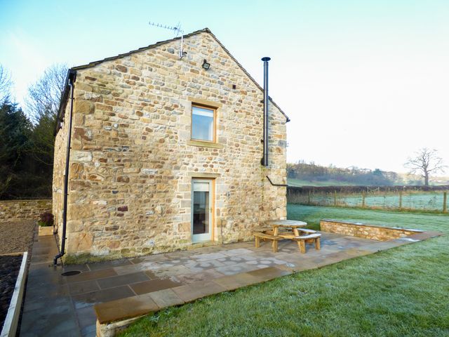 A stone house with a patio and round wooden picnic table in a grassy yard at Cow Hill Laith Barn in Bolton-by-Bowland