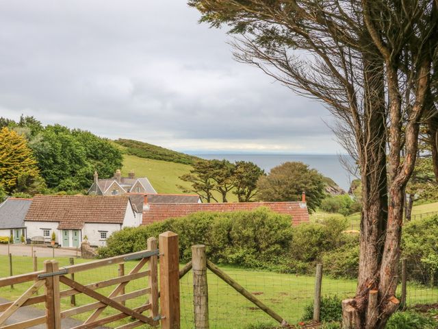 A countryside scene with houses trees a wooden gate and a view of the sea at Wren Cottage in Ilfracombe