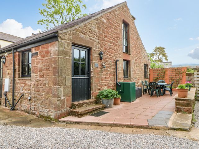A stone building with black framed windows and door and a patio with green chairs and table at The Old Byre in Appleby-in-Westmorland