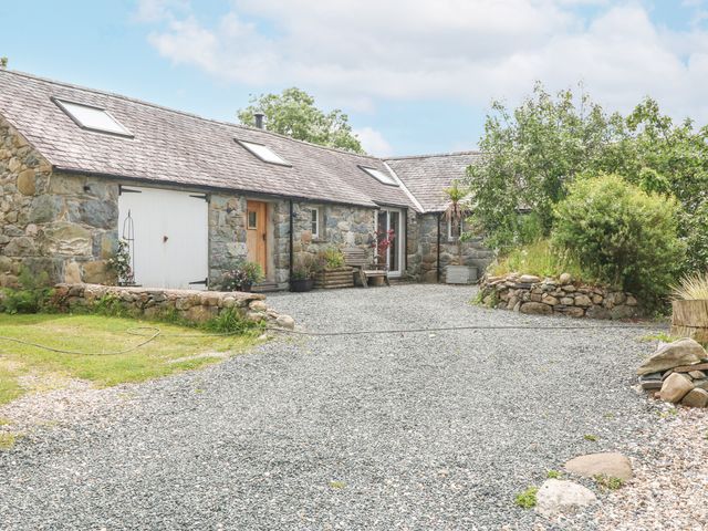 An exterior view of a stone cottage with a gravel driveway and surrounding greenery at Beudy'r Wennol in Groeslon