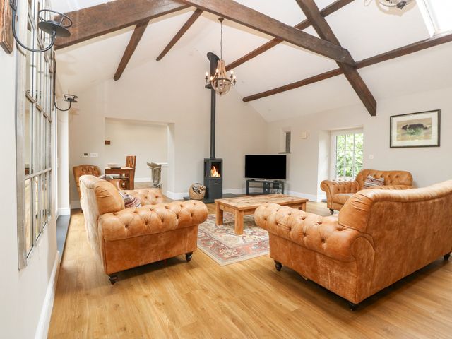 A living room with brown leather sofas a wooden coffee table a fireplace a television and exposed ceiling beams at Beudy'r Wennol in Groeslon