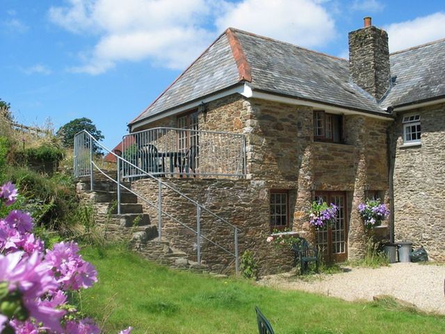 A stone house with an elevated terrace and metal railing with flowers in front at East Bickleigh in Halwell