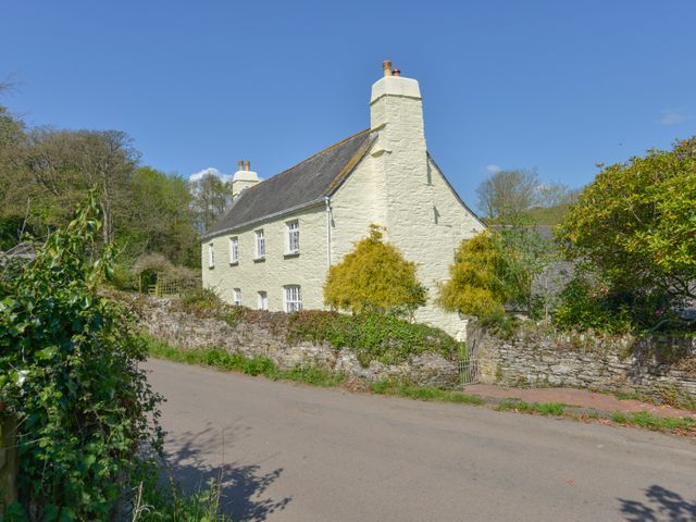 A stone house with chimneys behind a stone wall and gate along a country road at Tregonhawke Farmhouse in Millbrook