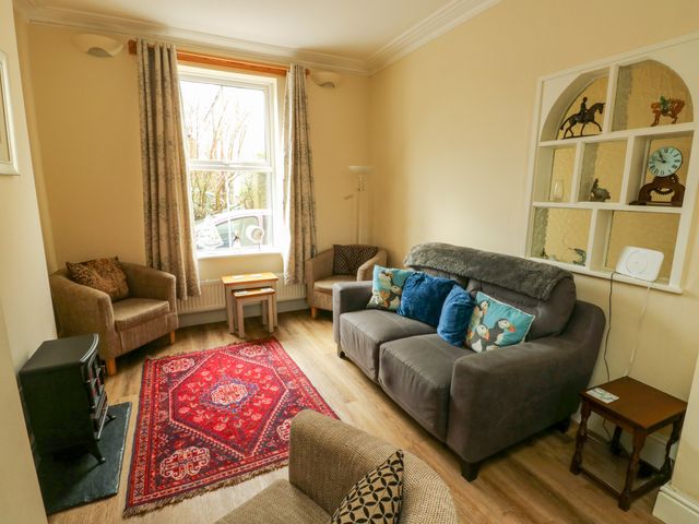 A living room with a sofa and armchairs around a red rug and a window at 1 Castle Row in Beaumaris