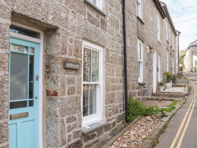A stone cottage with a blue door and a sign reading Mermaid on a street with a stone border and plants at Mermaid Cottage in Mousehole