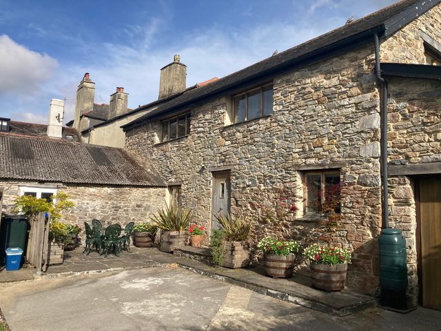 An outdoor area with a stone building, table, chairs, and planters at Old Armoury Barn Ashburton