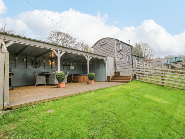 An outdoor covered patio with chairs a table and a hot tub next to a wooden cabin on a lawn at Shepherds Cabin at Titterstone in Clee Hill