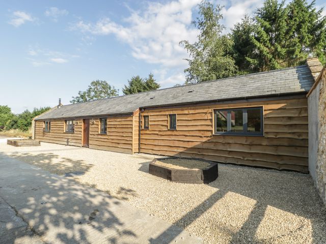 An exterior view of a single-story wooden building with gravel ground and trees in the background at The Milking Barn in Yeovil Somerset