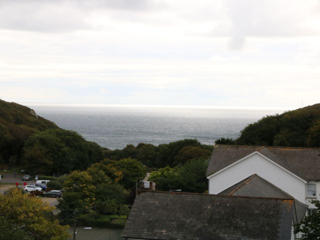 A view of the ocean with hills on either side trees and rooftops of houses in the foreground at The Watch in Porthcurno