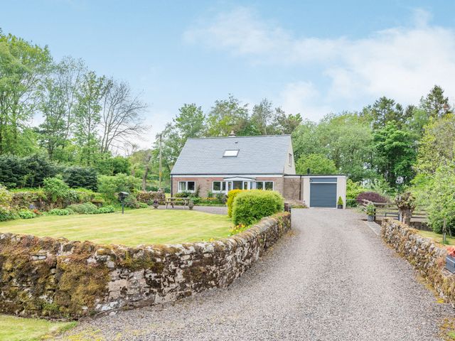 A detached house with a gravel driveway and stone wall surrounded by trees and grass at Falla Farmhouse in Jedburgh