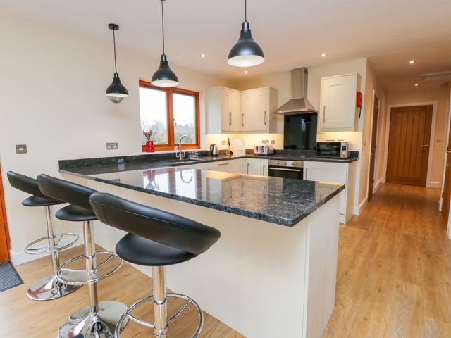 A kitchen with a black granite island countertop and black bar stools at Oak Lodge in Sheriff Hutton