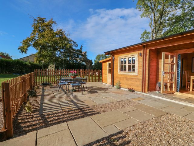 A wooden cabin with open door next to a fenced patio with table and chairs at Tythe Lodge in Howell near Heckington