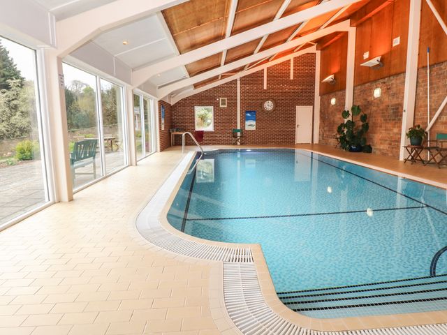An indoor swimming pool with tiled floor and large windows at Wood View Cottage in Blackawton