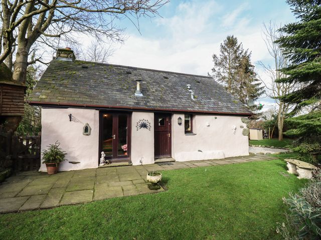 An exterior of a small cottage with a slate roof lawn and trees at Hafoty Boeth Cottage in Corwen