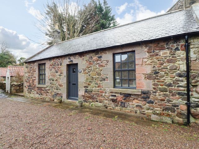 Exterior stone wall of a small house with two windows and a door at Bracken Lodge in Wooler