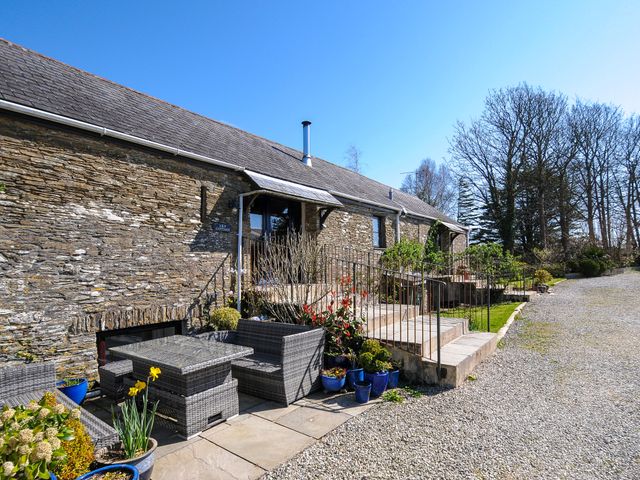 An outdoor patio area with wicker furniture and potted plants next to a stone house with stairs and railing at Lily Cottage in Looe