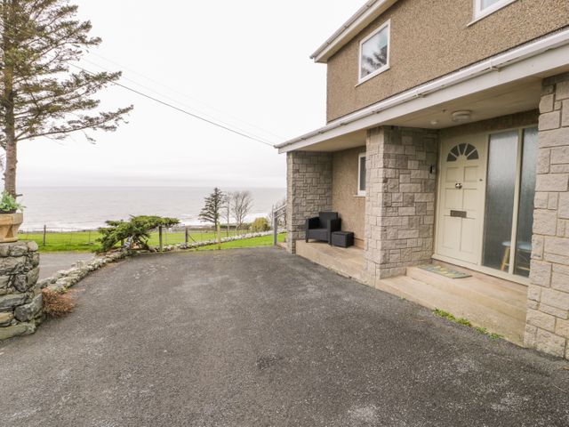 The front entrance of a house with stone pillars a driveway and outdoor seating overlooking the sea at Hendre Wylan in Llanaber