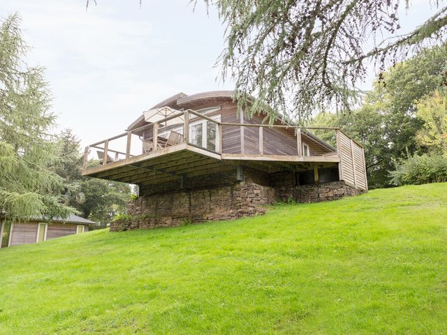 A wooden cabin with a deck and outdoor furniture on a grassy hillside with trees at 6 Lake View in Lanreath