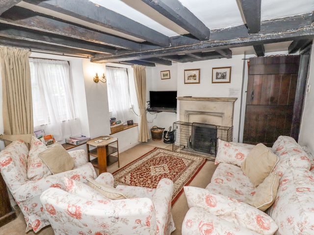 A living room with floral sofas a patterned rug a fireplace and wooden ceiling beams at Newbury Cottage in Bourton-On-The-Water