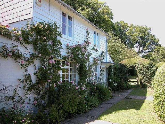 A white house with climbing plants and flowers along a path leading to a garden gate at Gun Hill Cottage in Heathfield